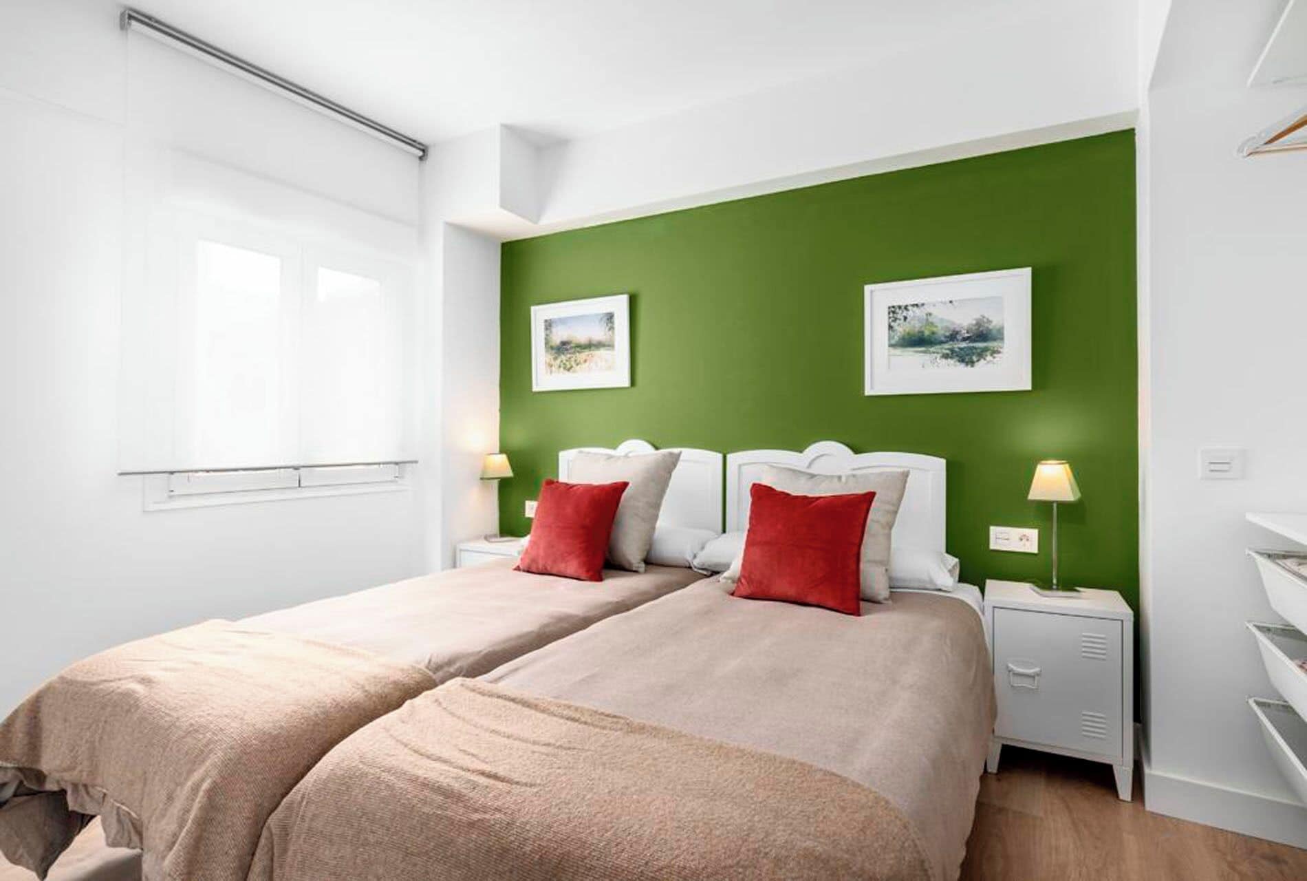 Een tweepersoonsbed met twee kussens, een nachtkastje met een lamp en een groene accentmuur.