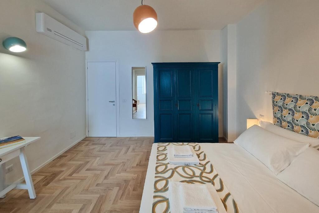 A bedroom with a bed, a desk, a wardrobe, and an air conditioning unit.