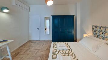 A bedroom with a bed, a desk, a wardrobe, and an air conditioning unit.
