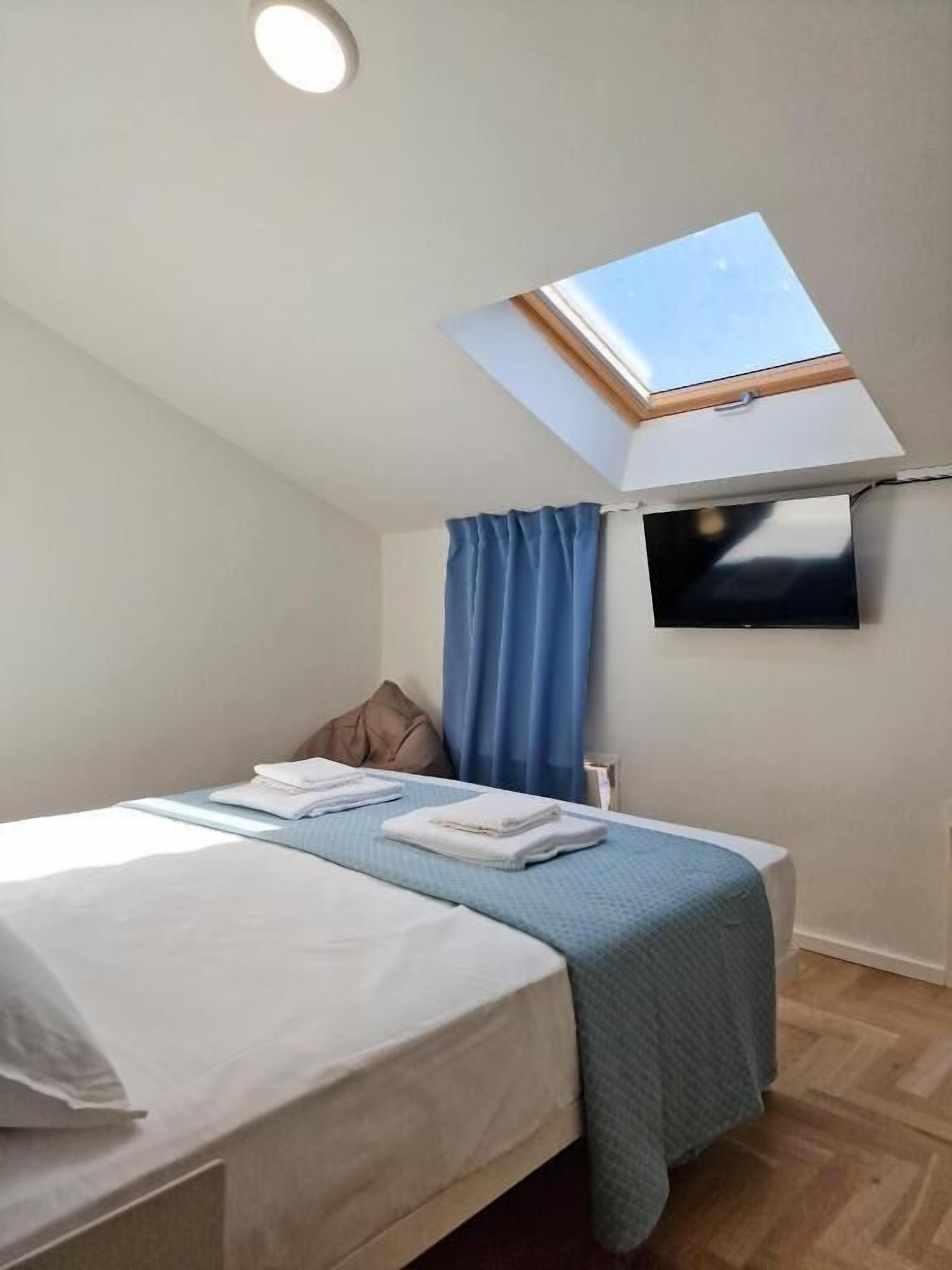 A bedroom with a skylight, a bed, a TV, and a window with curtains.