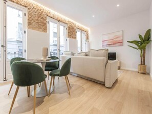 A modern living room with a sofa, two green chairs, a dining table, and a TV. - Chic Madrid Central Apartment (Madrid)