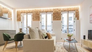 Ein modernes Wohnzimmer mit einer Couch, einem Couchtisch und einem Fernseher. Fenster bieten Blick auf die Stadt.