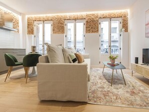 A modern living room with a sofa, a coffee table, and a TV. There are windows with a view of the city. - Chic Madrid Central Apartment (Madrid)