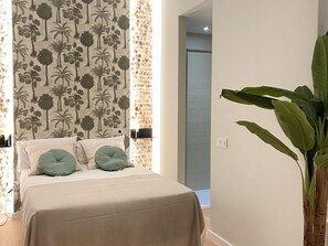 A bedroom with a bed, a large plant, and a wall with a palm tree pattern. - Chic Madrid Central Apartment (Madrid)