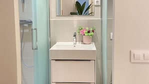 Ein Badezimmer mit Dusche, Waschbecken mit Spiegel und einer Zimmerpflanze.