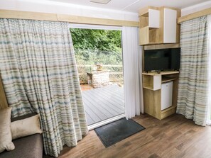 Una habitación con puerta corrediza de vidrio que da a una terraza exterior, estante empotrado para televisión y piso de madera.