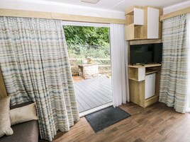 Una habitación con puerta corrediza de vidrio que da a una terraza exterior, estante empotrado para televisión y piso de madera.