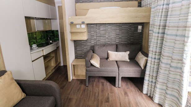 Una habitación pequeña con literas, kitchenette, sofá y cortinas.