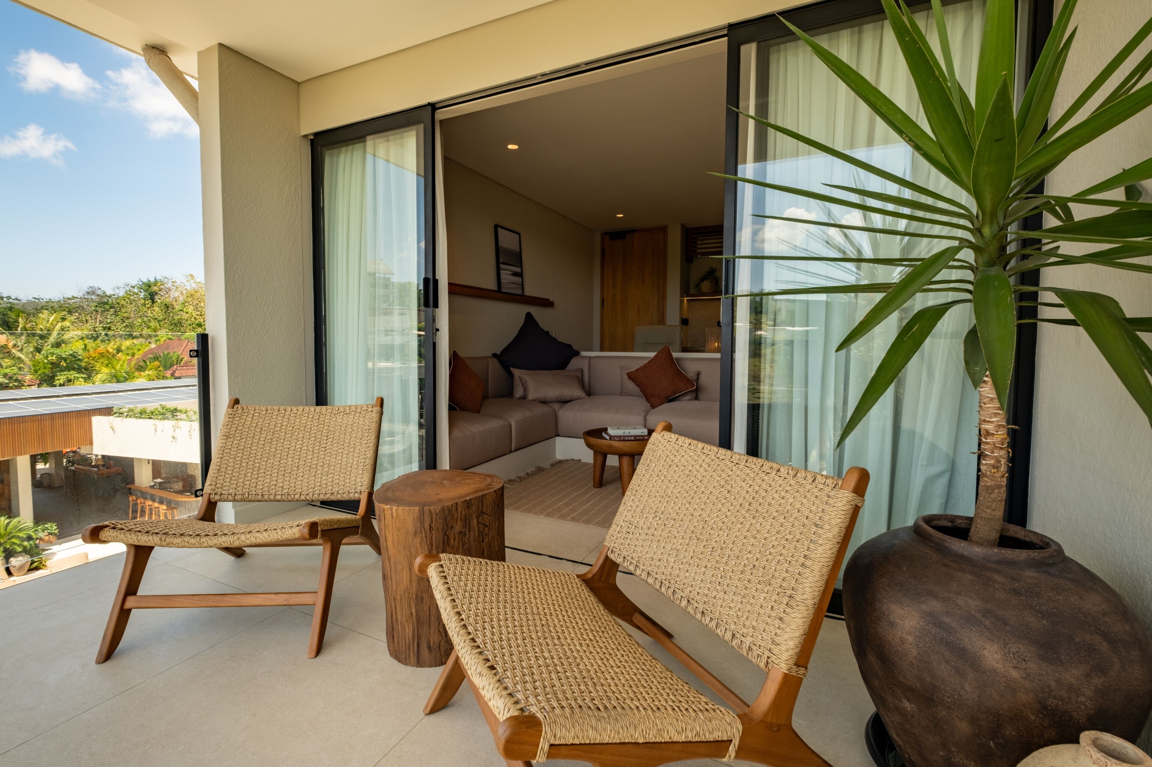 A balcony with wicker furniture, a large potted plant, and a view of the interior.