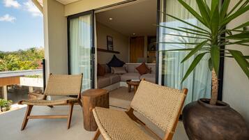 A balcony with wicker furniture, a large potted plant, and a view of the interior.