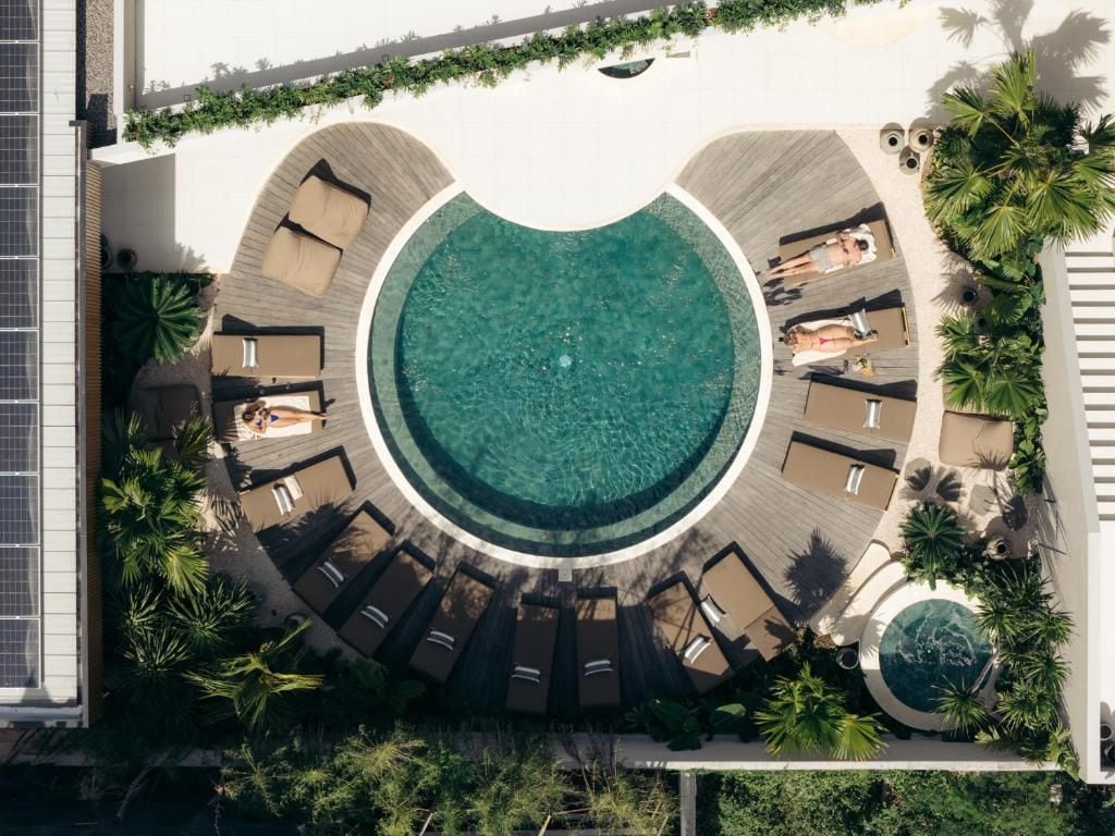 Una piscina circular con sillones de descanso y palmeras.