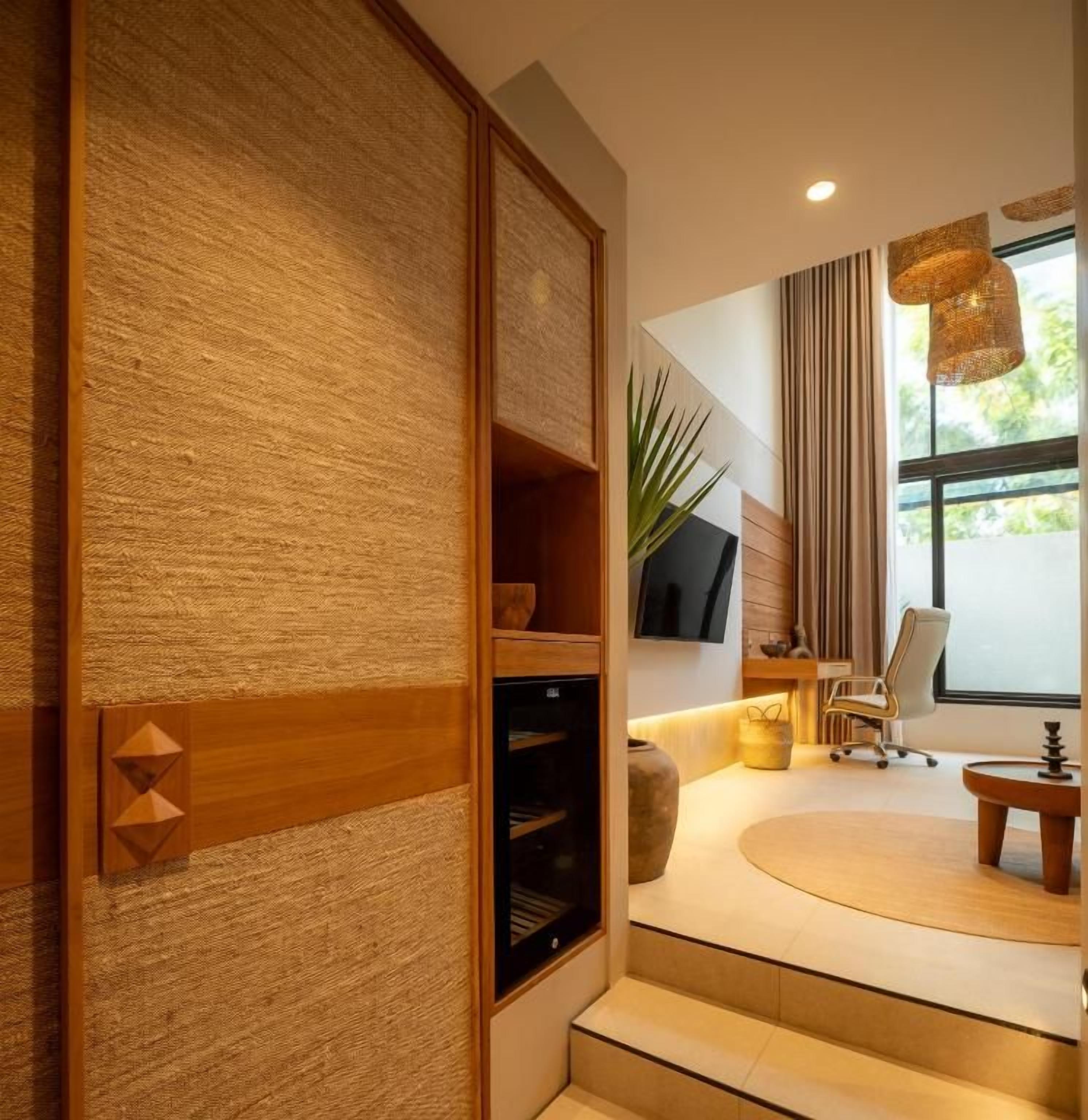 A modern interior with a wooden textured wall, a flat-screen TV, a comfortable seating area with a sofa and armchairs, and a large window with curtains.