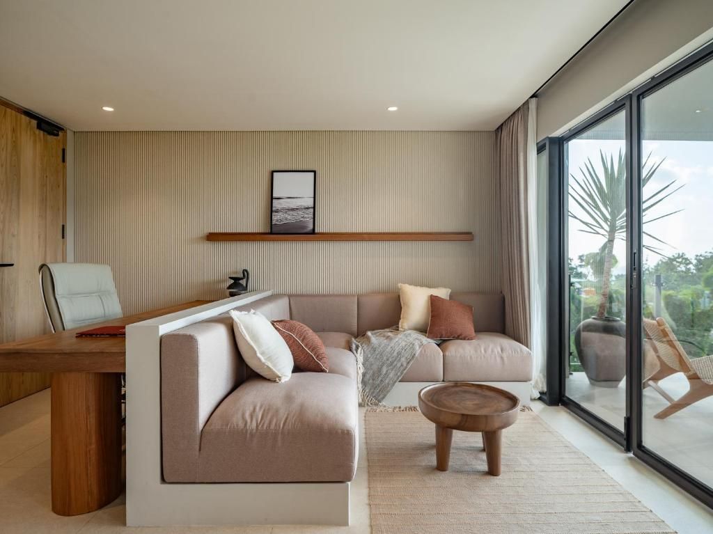 A modern living room with a sofa, a coffee table, and a desk. There is a large window providing a view outside.