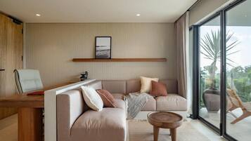 A modern living room with a sofa, a coffee table, and a desk. There is a large window providing a view outside.