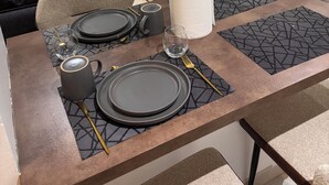 A dining area with a table set for four, a sofa, a TV, and a wooden cabinet. - Luxury Apartment with Pool in Saly – Quiet and Secure Residential Complex (Saly)