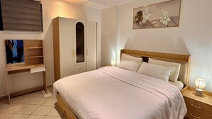 A bedroom with a bed, a wardrobe, a desk, and a painting on the wall. - Luxury Apartment with Pool in Saly – Quiet and Secure Residential Complex (Saly)