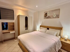 Ein Schlafzimmer mit einem Bett, einem Kleiderschrank, einem Schreibtisch und einem Bild an der Wand.