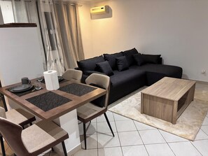 Ein modernes Wohnzimmer mit einer schwarzen Couch, einem Holztisch und einem Essbereich mit gedecktem Tisch für zwei Personen.
