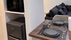 A compact kitchen with a microwave, refrigerator, and dining area set for two with plates, cutlery, and glasses. - Luxury Apartment with Pool in Saly – Quiet and Secure Residential Complex (Saly)