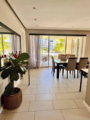 A spacious room with a dining area, large windows, and a potted plant. - Luxurious Secure 2 Bedroom V&A Waterfront Apt (Cape Town)