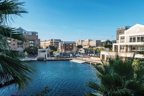 A waterfront view with modern buildings, a dock, and palm trees. - Luxurious Secure 2 Bedroom V&A Waterfront Apt (Cape Town)