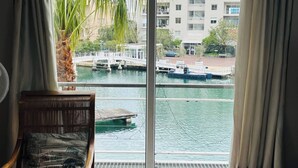 Ein Zimmer mit Blick auf ein Gewässer, ein Sessel mit gemustertem Kissen und ein Fenster mit Vorhängen.