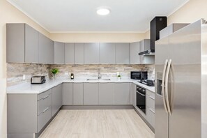 Une cuisine moderne avec des meubles gris, un réfrigérateur en acier inoxydable, un four à micro-ondes, un grille-pain et un évier.