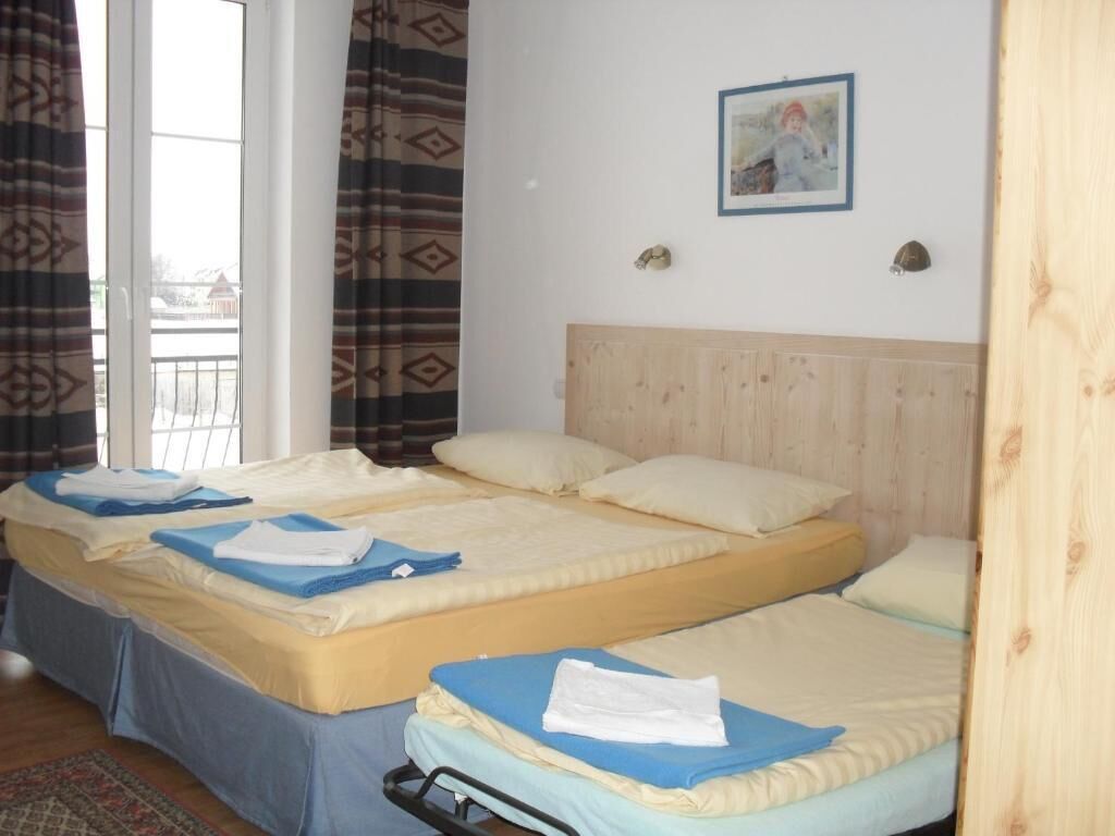 Une chambre d’hôtel avec trois lits, une tête de lit en bois, un tableau encadré au mur et une vue à travers une porte vitrée.