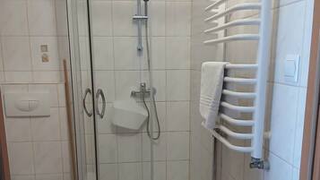 Cabina de ducha con paredes de azulejos blancos, toallero blanco y un inodoro blanco.