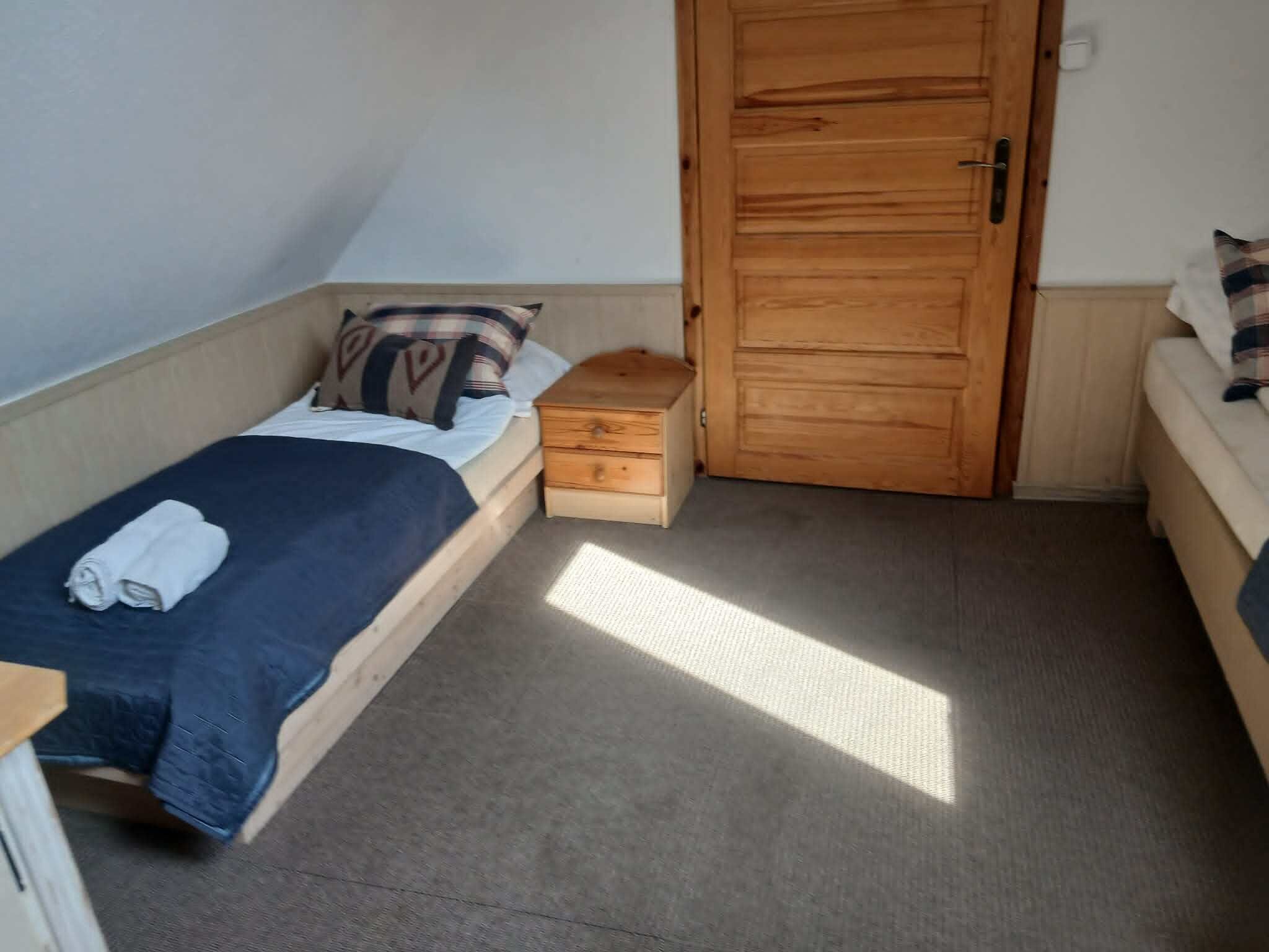 A small room with a single bed, a wooden nightstand, a wardrobe, and a small table.