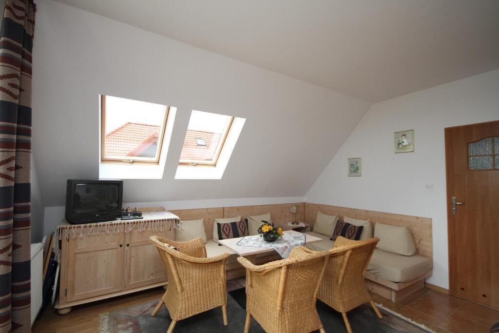 A cozy room with a sofa, two wicker chairs, a small table with a vase, a television on a cabinet, and two skylights.