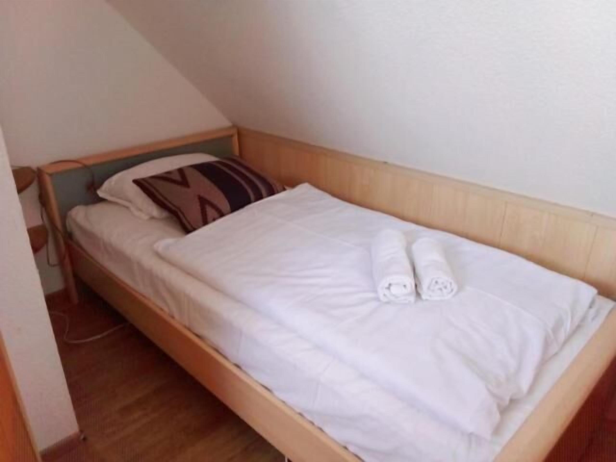 Una cama individual con cabecera de madera, ropa de cama blanca y una toalla enrollada.