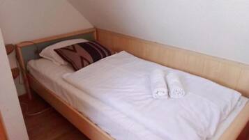 Una cama individual con cabecera de madera, ropa de cama blanca y una toalla enrollada.