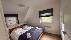 A bedroom with a bed, a window, a radiator, and a door.