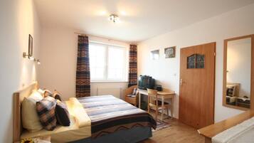 Een slaapkamer met een bed, een bureau, een televisie en een deur.