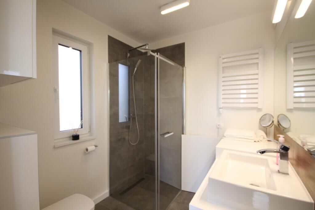 A modern bathroom with a glass-enclosed shower, a white sink, and a window.