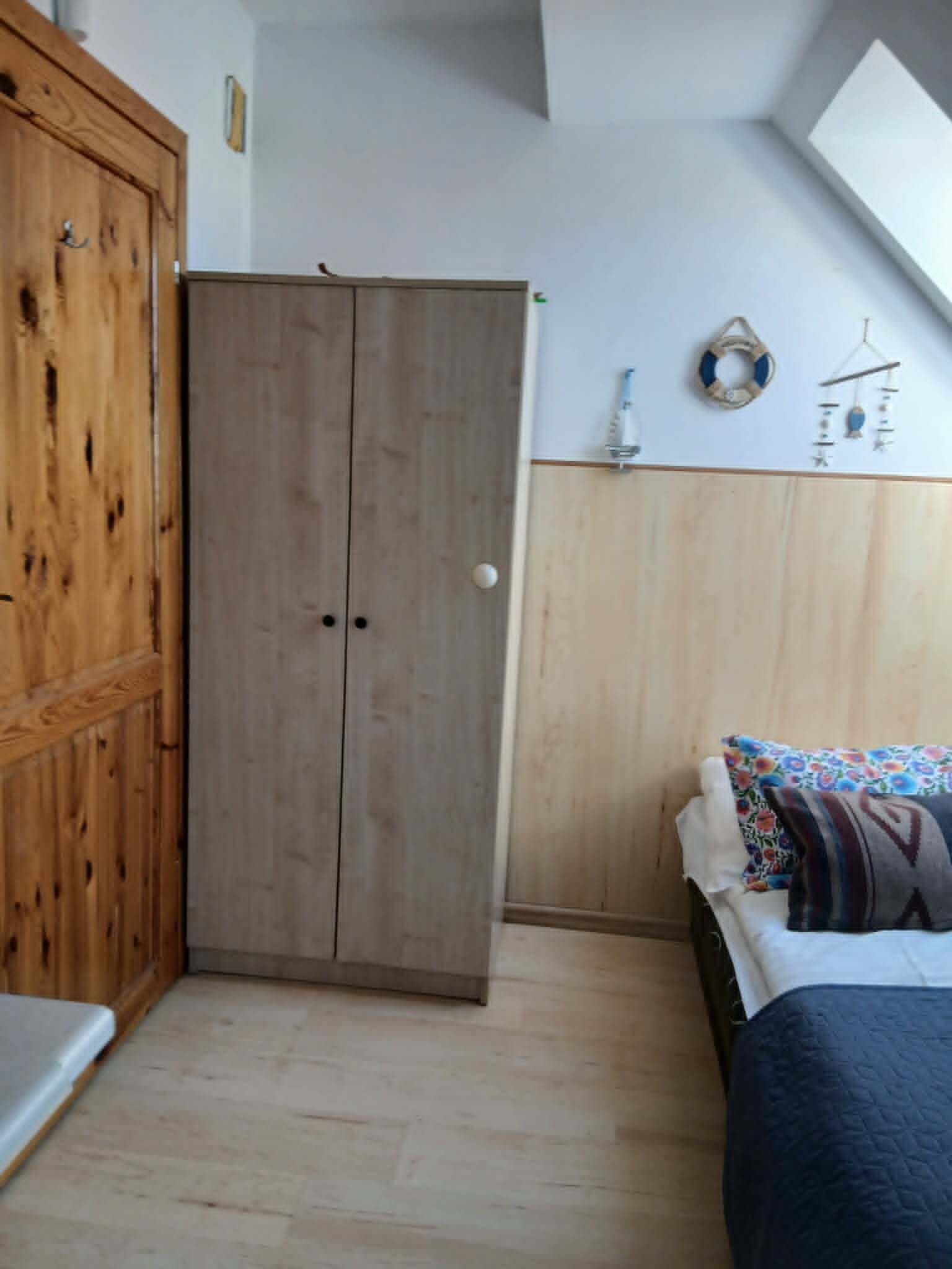 Et soveværelse med et træskab, en seng med mønstrede puder og en dekoration på væggen.