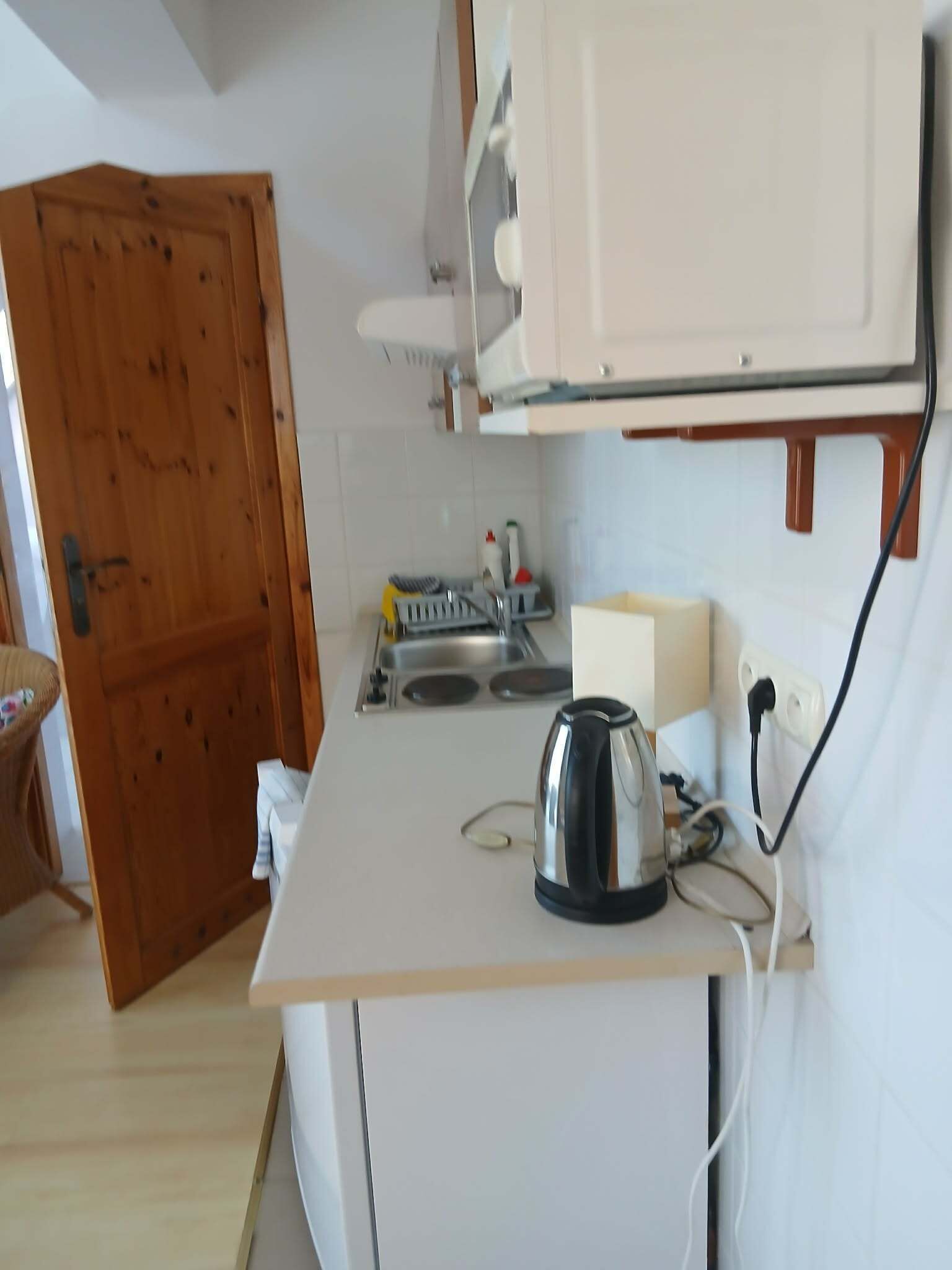 Cocina compacta con hervidor, pileta y puerta de madera.