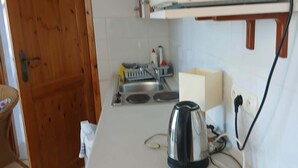 A compact kitchen with a kettle, a sink, and a wooden door.