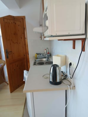 Une petite cuisine équipée d’une bouilloire, d’un évier et d’une porte en bois.