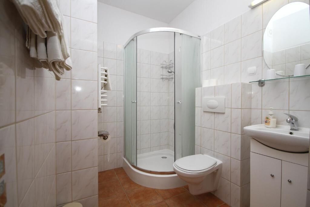 Un baño con cabina de ducha de vidrio, inodoro, lavamanos con espejo y un perchero para toallas.