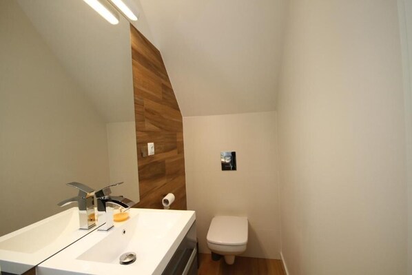 A bathroom with a white sink, chrome faucet, wooden panel wall, white toilet, and a small picture on the wall.