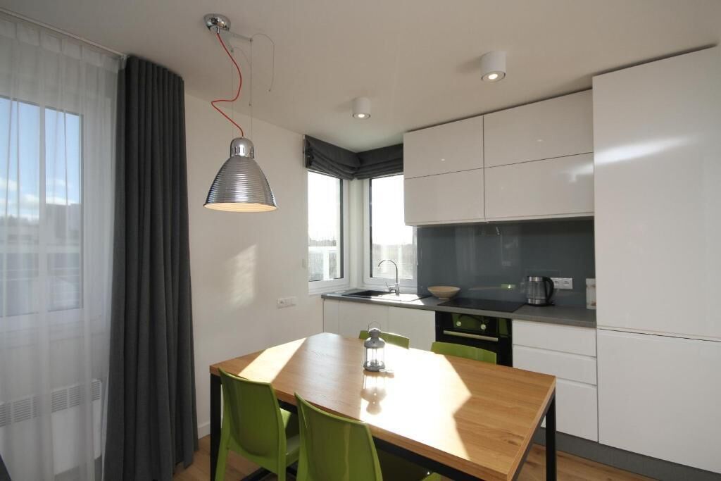 A modern kitchen with white cabinets, a wooden dining table, and a pendant light.