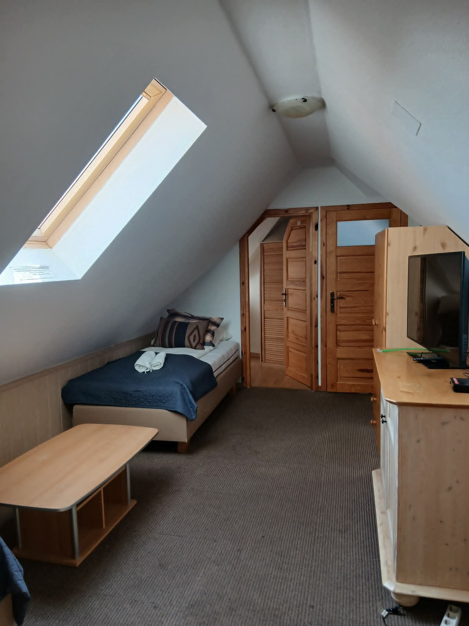 A small, sloped room with a bed, a desk, and a wardrobe.