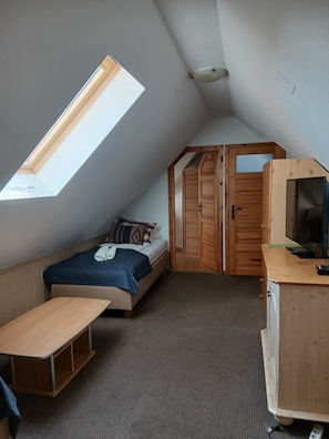 A small, sloped room with a bed, a desk, and a wardrobe.