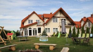 A residential building with a red-tiled roof, a patio with outdoor furniture, and a play area with a swing set and a slide.