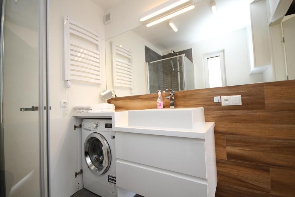 A compact bathroom with a washing machine, a sink, and a mirror.