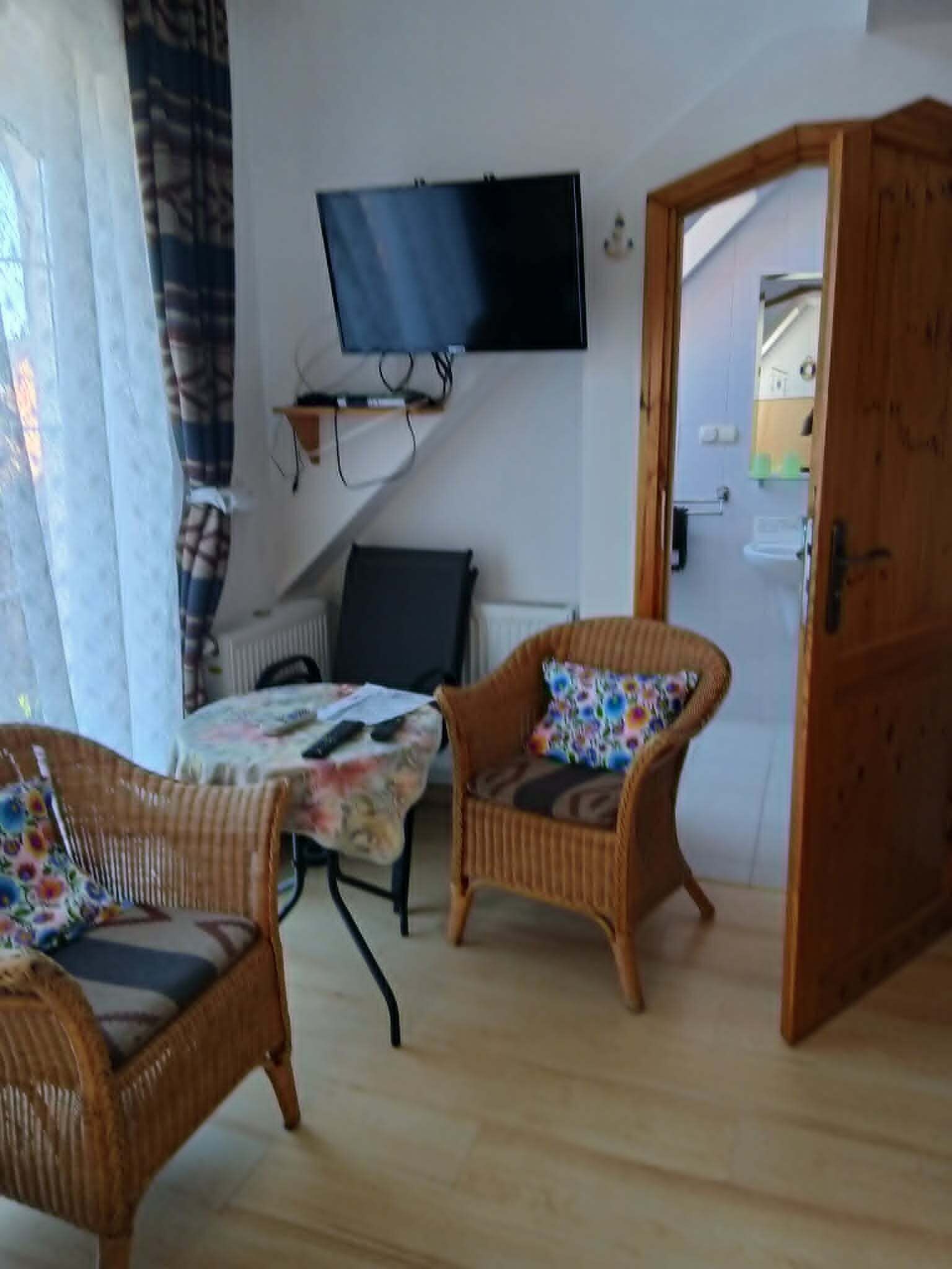 A room with wicker furniture, a television mounted on the wall, and a door leading to another room.