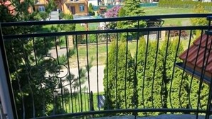 A balcony with a metal railing, a tiled floor, and a view of houses and greenery.