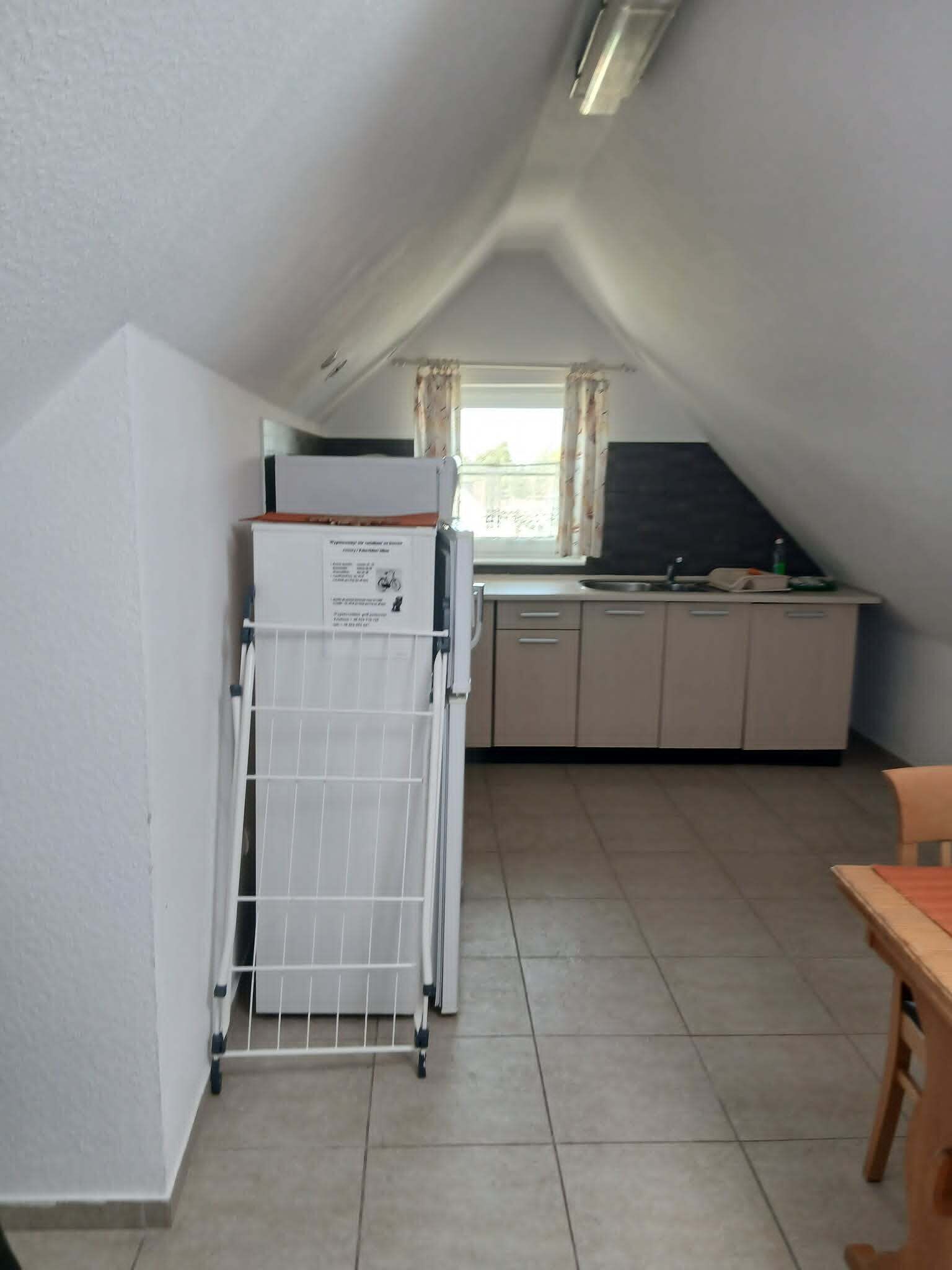A compact kitchen with a refrigerator, a sink, and a window with curtains.